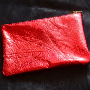 May include: A red leather clutch with a gold zipper. The clutch has a textured surface and a shiny finish.