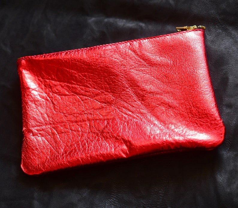 May include: A red leather clutch with a gold zipper. The clutch has a textured surface and a shiny finish.