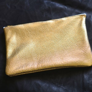 May include: A gold leather clutch purse with a zipper closure.