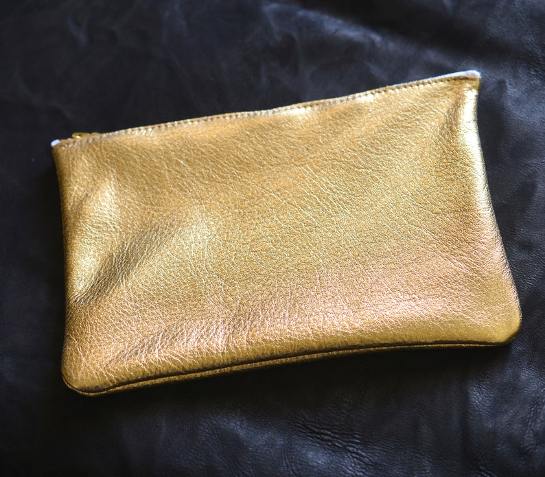 May include: A gold leather clutch purse with a zipper closure.