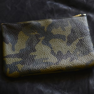 May include: A green, black, and brown camouflage patterned leather pouch with a gold zipper.