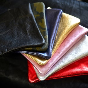 May include: A stack of colorful leather wallets in various shades of pink, gold, silver, black, and green. The wallets are arranged in a fan shape, with the black wallet on top.