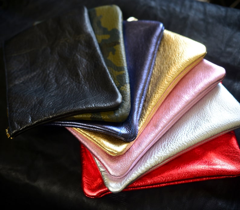 May include: A stack of colorful leather wallets in various shades of pink, gold, silver, black, and green. The wallets are arranged in a fan shape, with the black wallet on top.