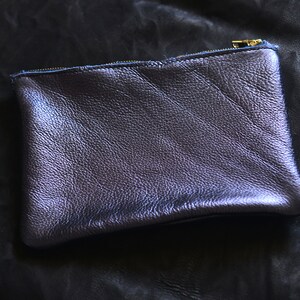 May include: A small, dark purple leather pouch with a zipper closure. The pouch is made of a textured leather and has a subtle sheen.
