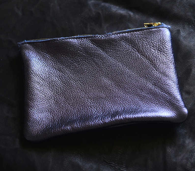May include: A small, dark purple leather pouch with a zipper closure. The pouch is made of a textured leather and has a subtle sheen.