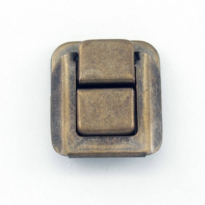 May include: Antique brass latch with a square shape and a textured finish. The latch has a hinged top and a sliding bottom.