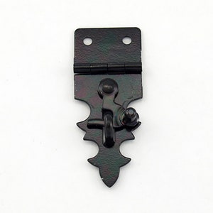 May include: A black metal latch with a decorative, pointed bottom and a hinged top with two holes. The latch features a lever and a round knob for securing. The hardware has a distressed finish.