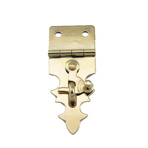 May include: A gold-toned metal latch with a decorative design. The latch has a hinged top and a spring-loaded lever with a ring.