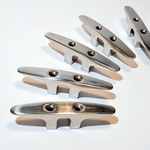 May include: Set of seven silver-toned stainless steel boat cleats. The cleats are arranged in a semi-circle pattern on a white surface.