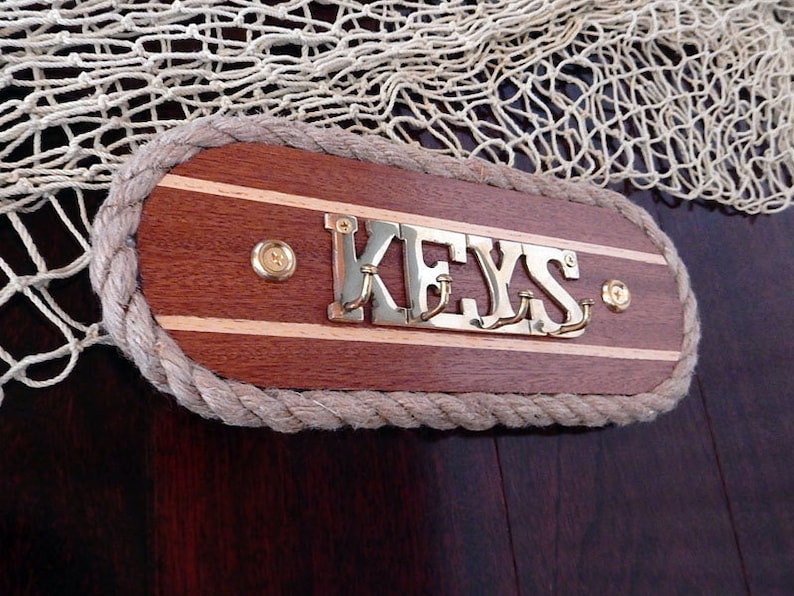 May include: Wooden key holder with a rope border and brass hooks. The holder has a light wood background with dark wood stripes and the word "KEYS" in brass letters.