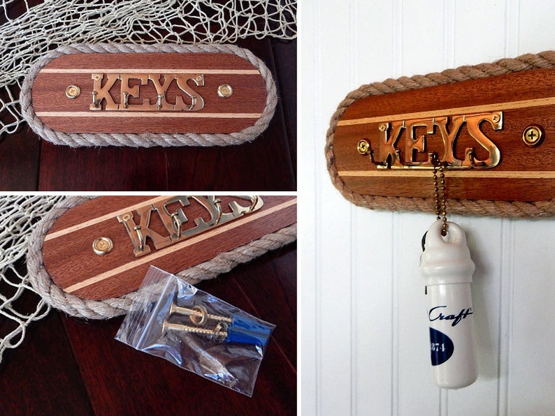 May include: A wooden key holder with a rope border and the word "KEYS" in brass letters. The holder is mounted on a white wall with a white ceramic bottle stopper hanging from it.