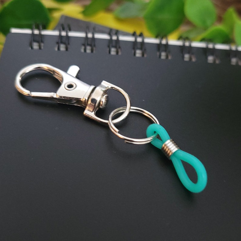 May include: A silver key chain with a teal rubber loop. The key chain has a split ring and a lobster claw clasp.