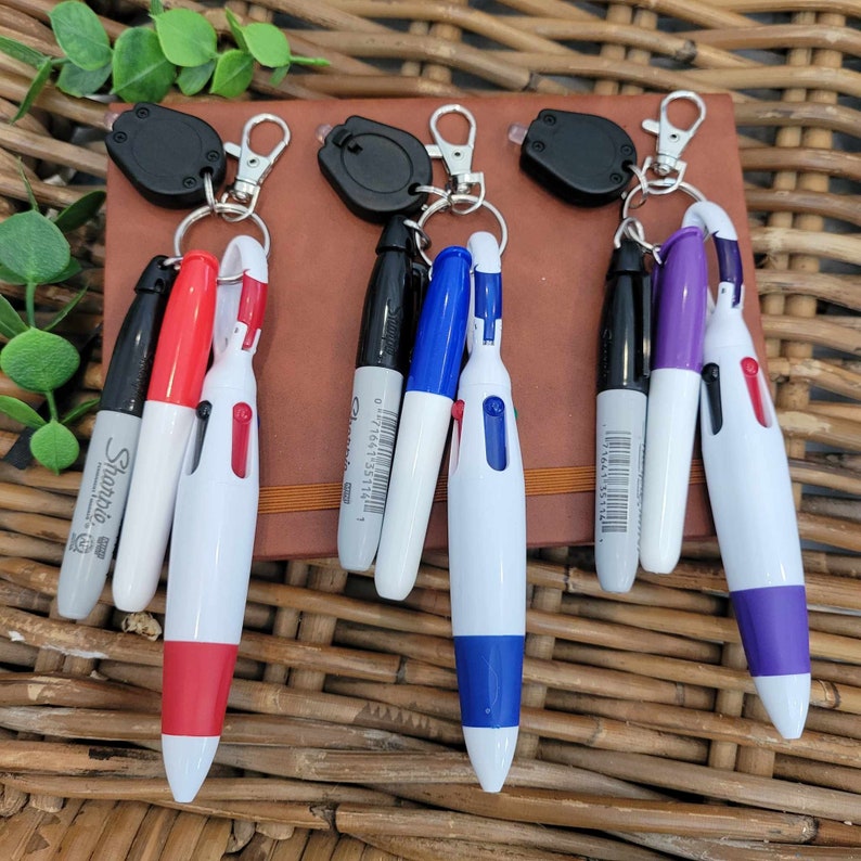 Pu&ograve; includere: Sei portachiavi con penne di diversi colori attaccate. I portachiavi sono neri con un anello argentato. Le penne sono nere, rosse, blu, viola e bianche con accenti neri e blu. Le penne sono tutte del marchio Sharpie.