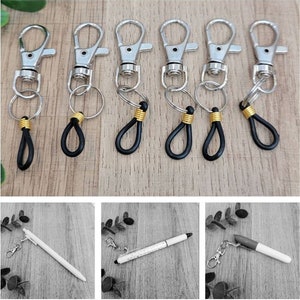 May include: Six silver keychains with black and gold accents. Each keychain has a silver ring and a black loop. The keychains are arranged in a row on a wooden surface.