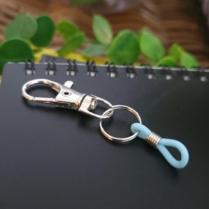 May include: A silver key chain with a light blue rubber loop. The key chain has a silver split ring and a silver clip.