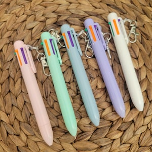 May include: Six multi-coloured retractable pens with keychains. The pens are in shades of pink, green, blue, purple, and white. The pens have multiple ink colours, including orange, green, and purple.