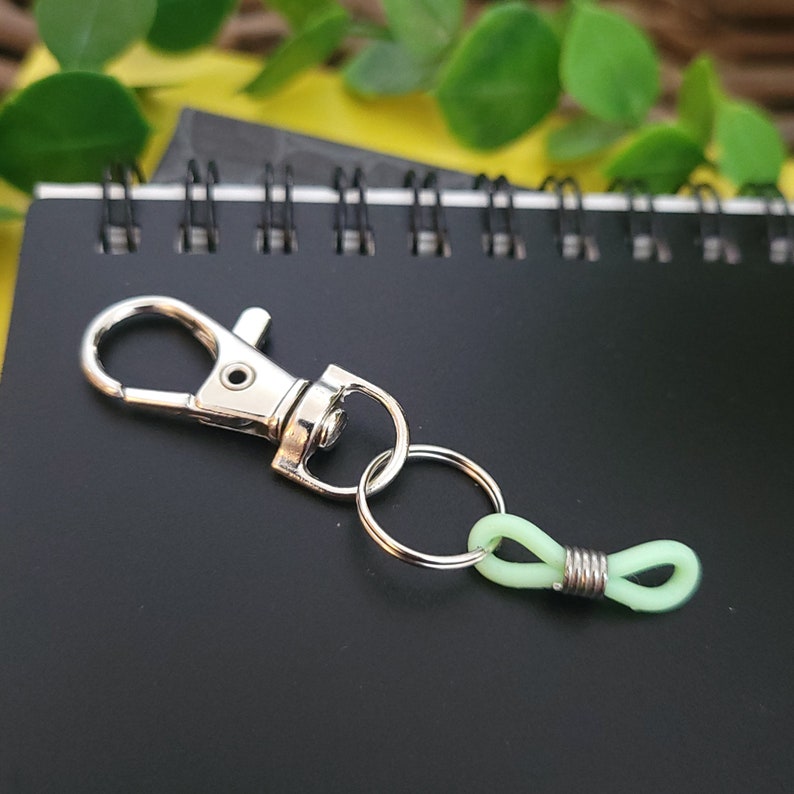 May include: A silver key chain with a silver clasp and a light green plastic loop.