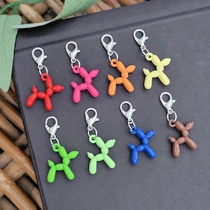 May include: A collection of eight colorful balloon dog charms. The charms are in various colors, including red, pink, orange, yellow, green, blue, and brown. Each charm has a silver-colored clasp.