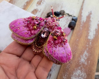 May include: A pink and gold embroidered moth brooch with crystal and bead embellishments.