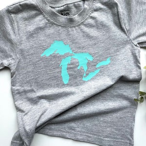May include: A grey t-shirt with a turquoise outline of the Great Lakes on the front. The shirt is made by Gerber Kids.