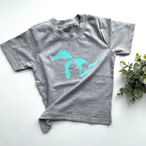 May include: A grey short-sleeved t-shirt with a turquoise outline of the Great Lakes on the front. The shirt has a tag that says "Carson's Kids".