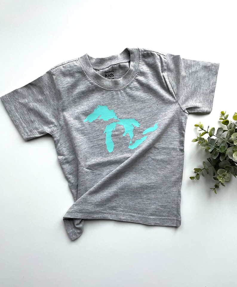 May include: A grey short-sleeved t-shirt with a turquoise outline of the Great Lakes on the front. The shirt has a tag that says "Carson's Kids".