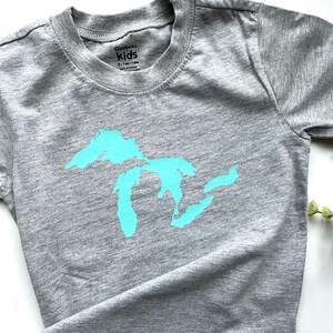 May include: Grey short-sleeved t-shirt with a light blue outline of the Great Lakes on the front. The shirt has the text "Gerber Kids" on the tag.