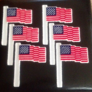 May include: Six small American flags on white sticks. The flags are red, white, and blue with a blue field of stars. The flags are arranged in two rows of three.