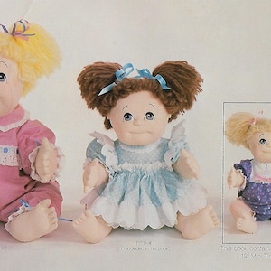 May include: Three Cabbage Patch Kids dolls, one 22 inches, one 18 inches, and one 12 inches. The dolls are wearing different outfits. The 12 inch doll is wearing a purple and white floral print dress. The 18 inch doll is wearing a blue and white polka dot dress with a white lace trim. The 22 inch doll is wearing a pink dress with a white lace trim and a blue bow. This book contains patterns for the 12 inch Mini Tiny Tot doll.