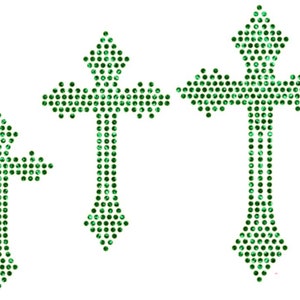 May include: Three green rhinestone crosses of varying sizes. The crosses are made of small, round rhinestones that are arranged in a cross shape. The crosses are all the same design, but they are different sizes. The largest cross is at the top of the image, and the smallest cross is at the bottom.