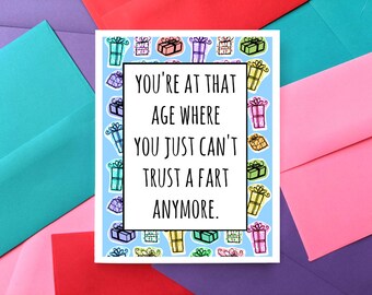 May include: A humorous birthday card with a blue background and a white border. The card features a pattern of colorful gift boxes and the text "You're at that age where you just can't trust a fart anymore."