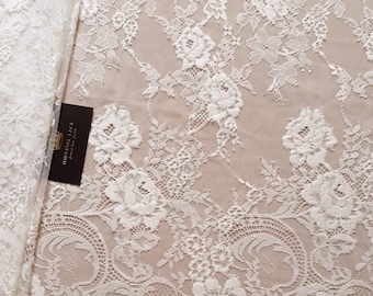 Puede incluir: Tela de encaje floral blanca con un patrón delicado. El encaje tiene una textura suave y fluida, ideal para manualidades, costura o decoración.