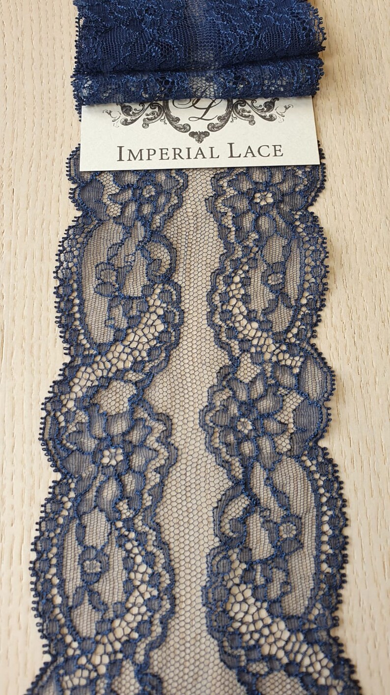 May include: Navy blue lace trim with a delicate floral pattern. The lace is shown folded in half, with the text "IMPERIAL LACE" visible on a white label.