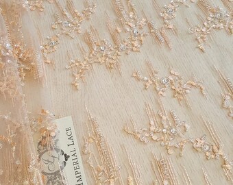 May include: Peach colored beaded lace fabric with a delicate floral pattern. The fabric has a sheer, lightweight feel and is perfect for creating elegant garments or accessories. The label reads "Imperial Lace".