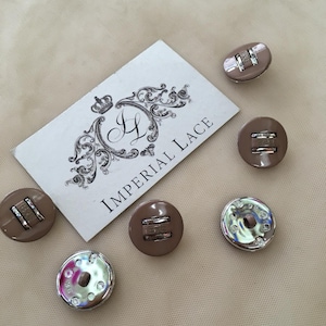 May include: Five round buttons in a muted taupe color with a central silver-toned metal bar detail. Two buttons show their shiny silver-toned metal backs with small circular indentations. A white rectangular card displays the text Imperial Lace.