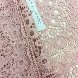 May include: Close-up of a pale pink lace fabric with a white label that reads "Imperial Lace".
