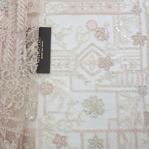 May include: A delicate, beaded lace fabric with a geometric pattern in shades of white and pink. The fabric features intricate floral designs and small sequins.