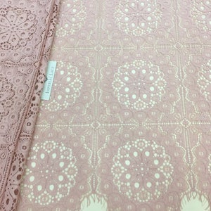 May include: Pink lace fabric with a delicate floral pattern and a fringed edge. The fabric is labeled "Imperial Lace".