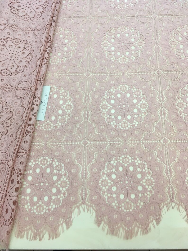May include: Pink lace fabric with a delicate floral pattern and a fringed edge. The fabric is labeled "Imperial Lace".