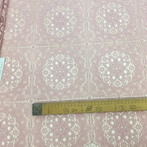 May include: Pink lace fabric with a delicate floral pattern. The fabric has a scalloped edge and is measured with a ruler in inches.