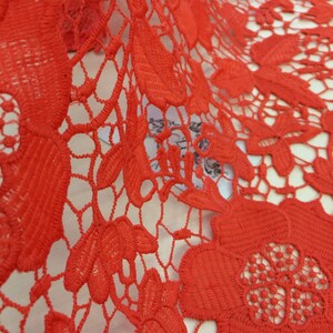 May include: Red crochet lace fabric with a floral pattern. The lace is delicate and intricate, with a fine mesh design.