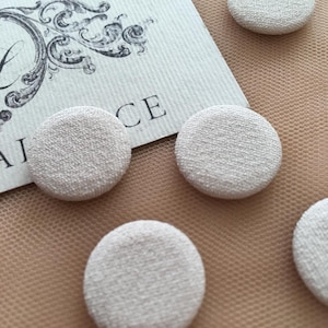 May include: Five off-white fabric covered buttons. The buttons are round and have a textured surface.