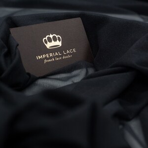 May include: A brown card with a gold crown and the text "IMPERIAL LACE french lace dealer" on a black fabric background.
