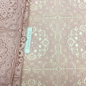 May include: Pink lace fabric with a delicate floral pattern. The fabric has a square grid pattern with a small floral design in each square. The fabric is labeled "Imperial Lace".