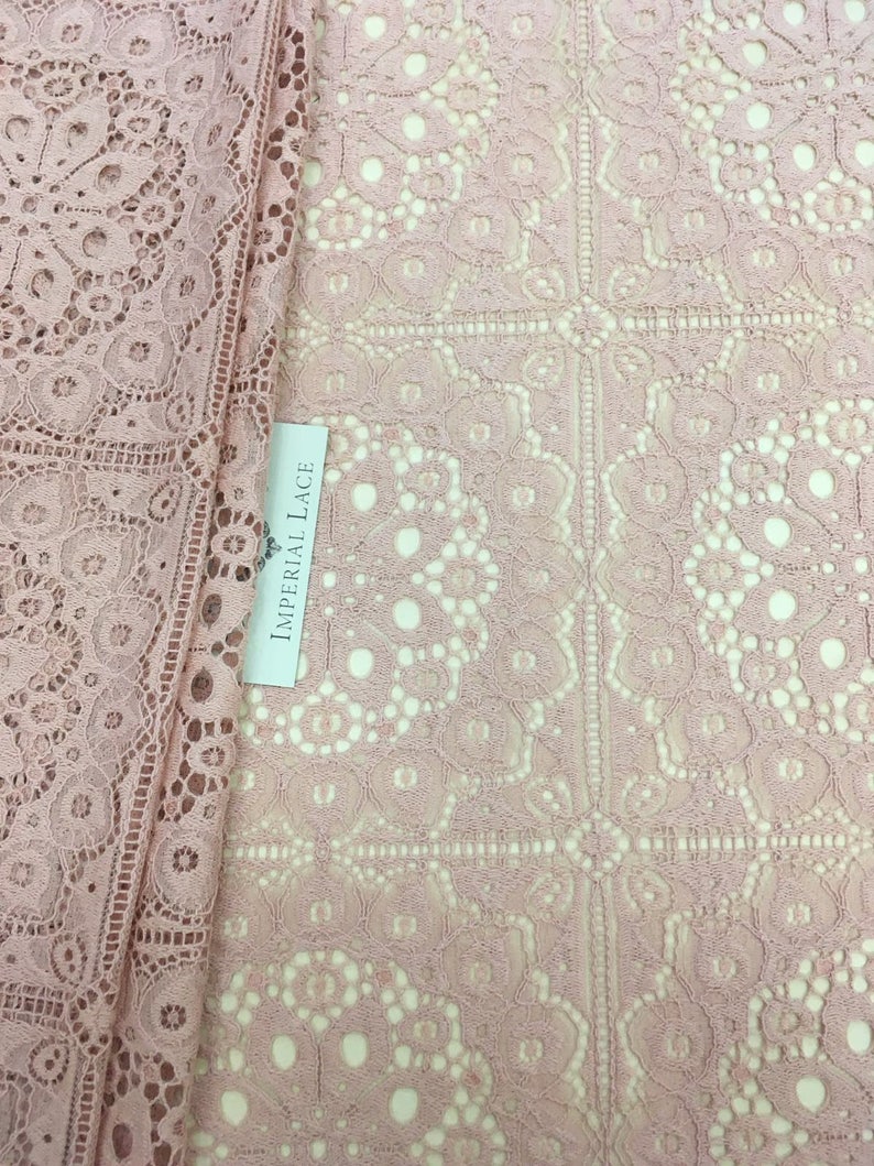 May include: Pink lace fabric with a delicate floral pattern. The fabric has a square grid pattern with a small floral design in each square. The fabric is labeled "Imperial Lace".