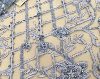 May include: Light blue lace fabric featuring a grid pattern, floral embroidery, and small beads. The fabric includes a tag with the text IMPERIAL LACE. The design consists of interconnected lines and detailed flower motifs embellished with iridescent beads.