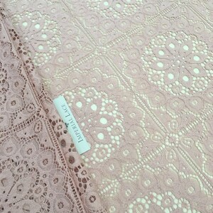 May include: Pale pink lace fabric with a delicate floral pattern. The fabric has a square grid pattern with a small circle in the center of each square. The label reads "Imperial Lace".