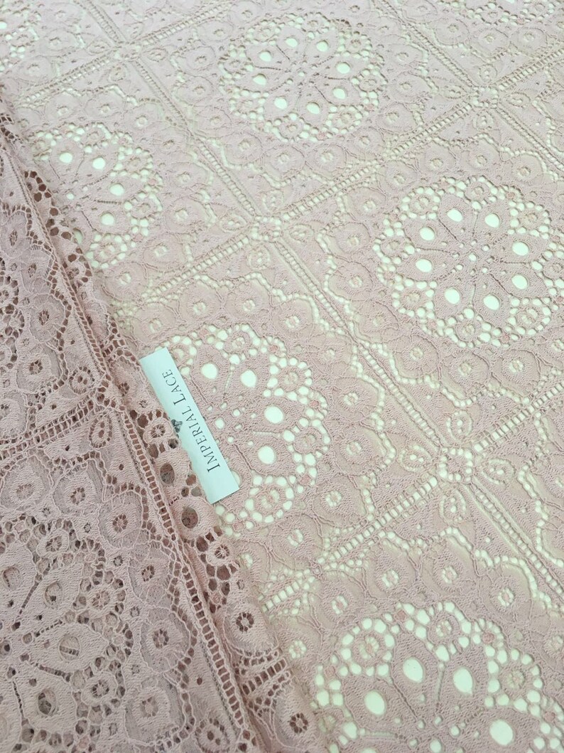 May include: Pale pink lace fabric with a delicate floral pattern. The fabric has a square grid pattern with a small circle in the center of each square. The label reads "Imperial Lace".