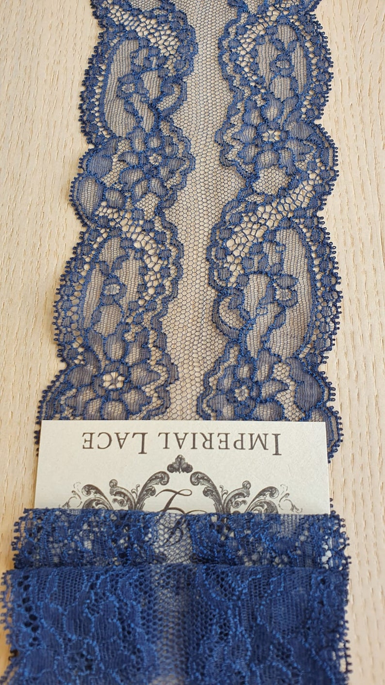 May include: Navy blue lace trim with a delicate floral pattern. The lace is shown folded in half and has a label that reads "Imperial Lace".