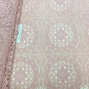 May include: Pink lace fabric with a delicate floral pattern and scalloped edges. The fabric has a square grid pattern with a circular design in each square. The label reads "Imperial Lace".